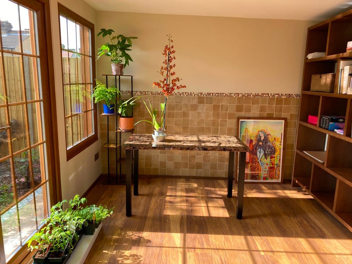 Sunlit garden room used as a study and plant room, with a marble-topped table and oak shelving